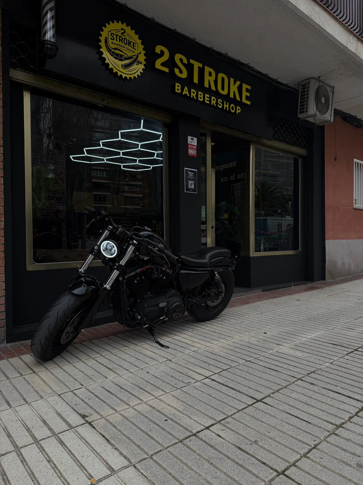 Fachada de 2 Stroke Barbershop en Fuenlabrada con una moto aparcada en la puerta