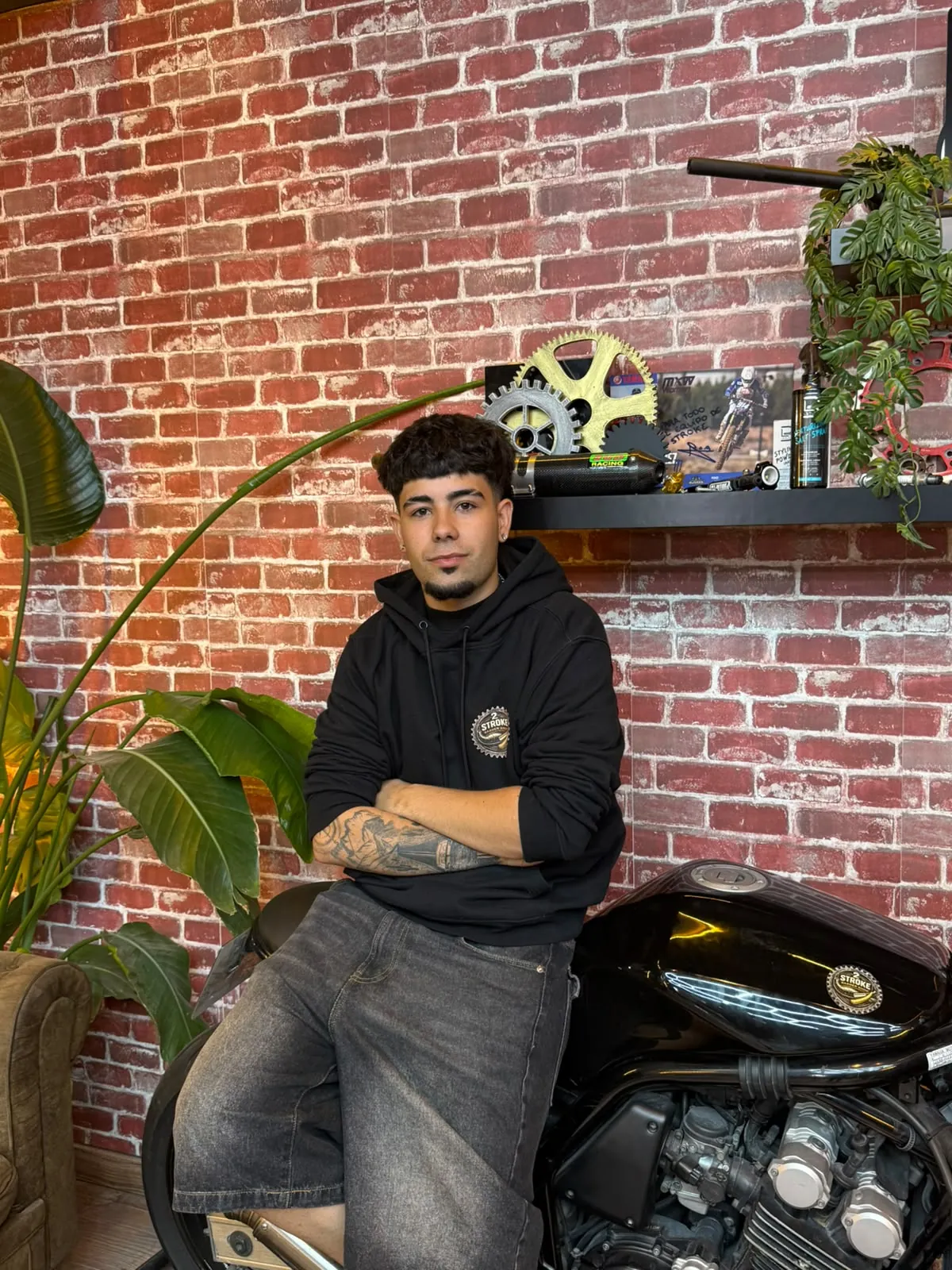 Iker, barbero de 2 Stroke Barbershop en Fuenlabrada, apoyado en la moto del local